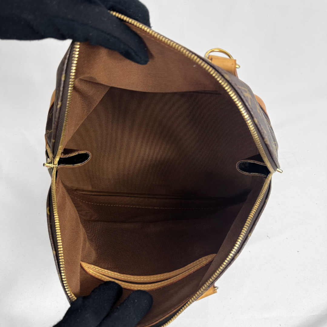 An open Louis Vuitton monogram handbag shown from above, revealing a brown striped interior lining with gold-tone zippers and hardware. Gloved hands are holding the bag open against a plain white background.