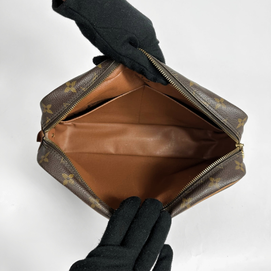 A Louis Vuitton monogram canvas toiletry bag shown open, held by black gloves against a plain white background.