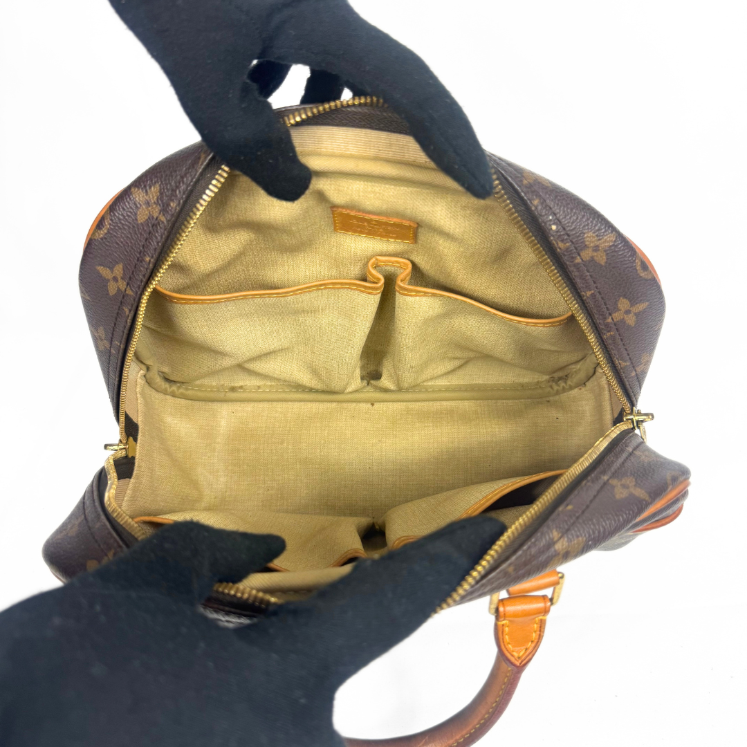 An open Louis Vuitton handbag in brown monogram canvas, shown from the inside with a black-gloved hand holding it open against a white background.
