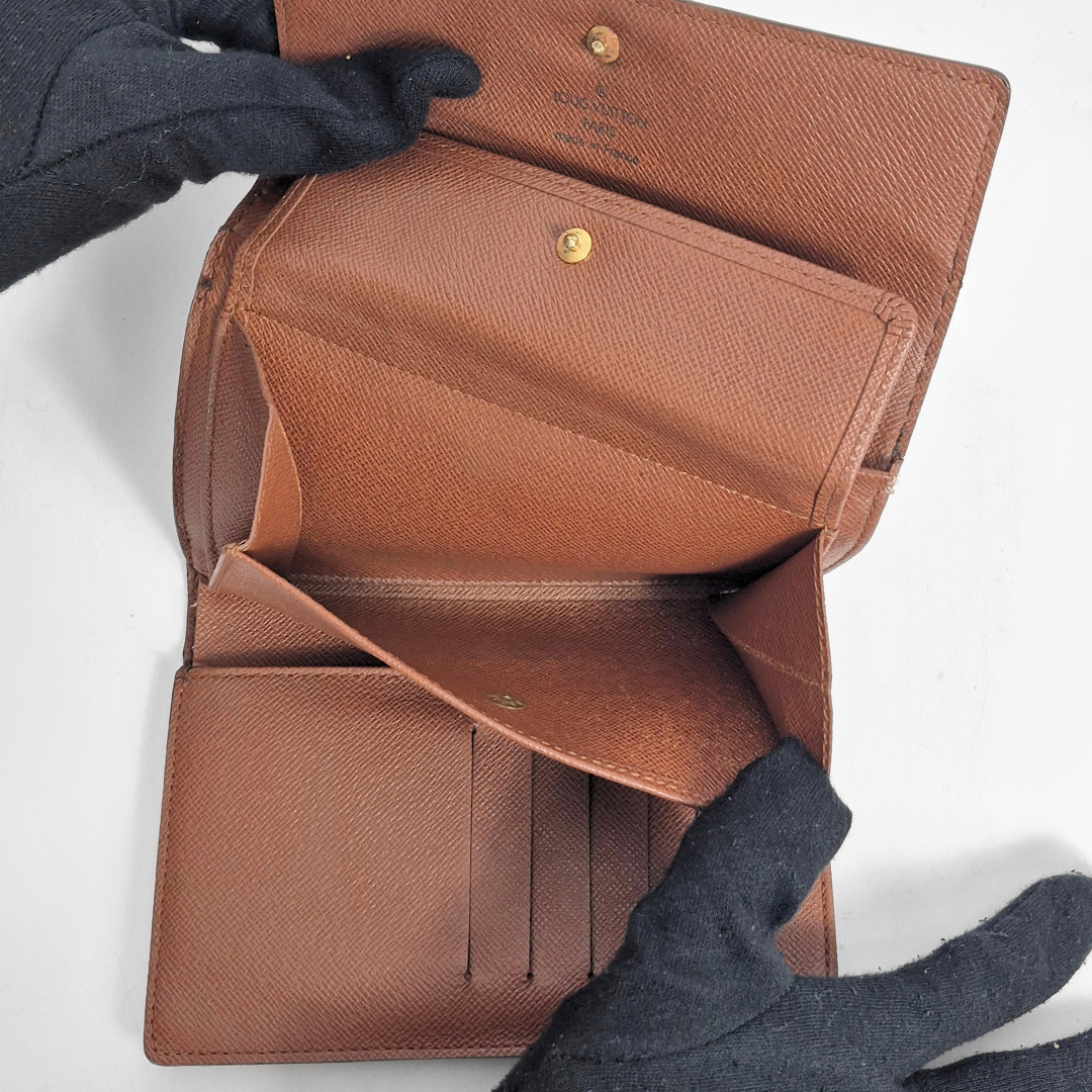 Cartera de cuero marrón abierta por una mano enguantada sobre un fondo blanco.