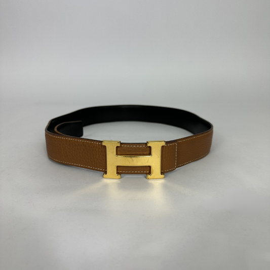 A classic brown leather belt with a gold-tone H buckle, displayed on a neutral light gray background.