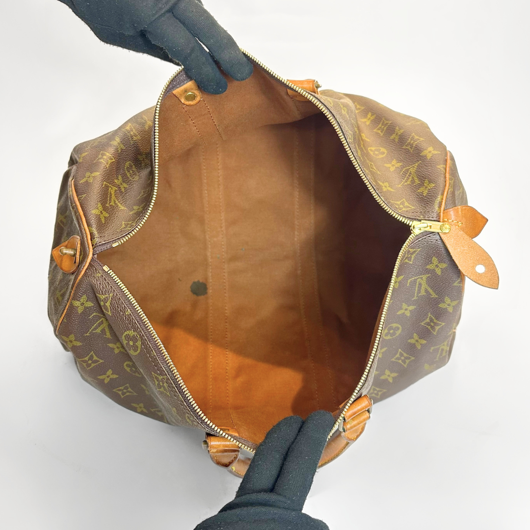 Brown leather bag with monogram pattern held open by a gloved hand on a white background