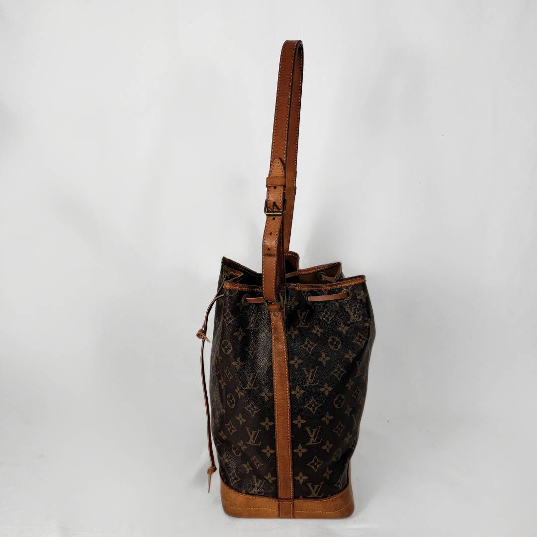 A Louis Vuitton monogram canvas bucket bag with brown leather trim and a single shoulder strap, photographed against a plain light gray background.