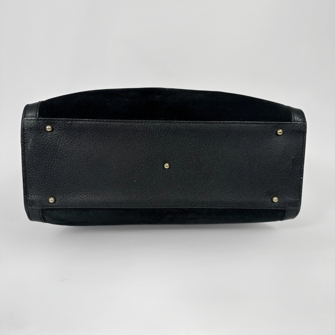 Black handbag with gold bamboo handles on a white background