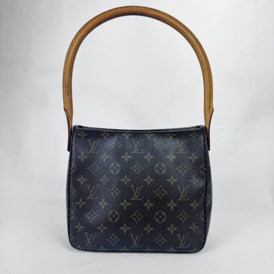 A Louis Vuitton axelväska i mörkmarinblå monogramcanvas med ett brunt läderhandtag upptill, fotograferad mot en ljusgrå studiobakgrund.