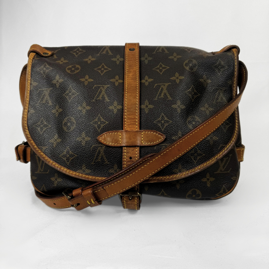 Louis Vuitton Bolso de hombro de lona con monograma, ribete y correa de cuero color camel, fotografiado sobre un fondo blanco liso.
