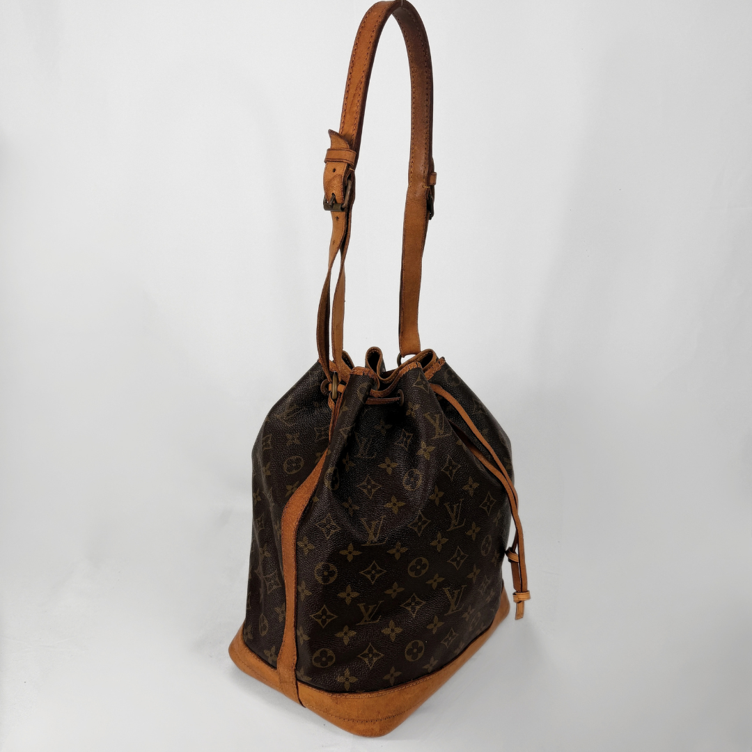 A Louis Vuitton monogram canvas bucket bag with tan leather trim, a drawstring closure, and a single shoulder strap, photographed against a plain white background.