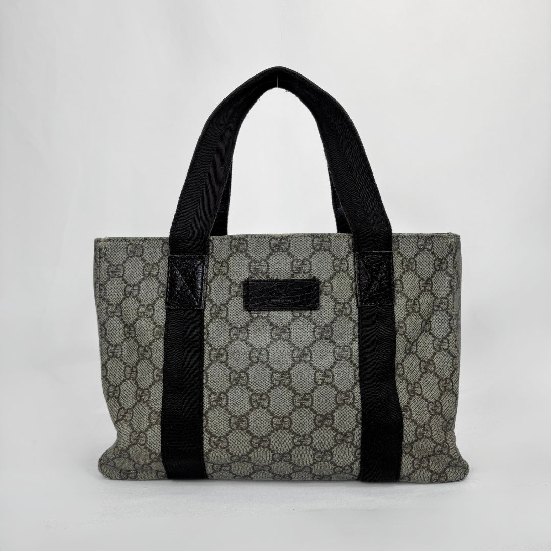 A vintage-style GG Supreme canvas tote bag in gray and brown monogram pattern with black fabric handles and trim, shown against a plain light gray background.