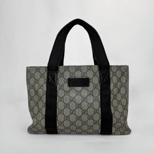 A vintage-style GG Supreme canvas tote bag in gray and brown monogram pattern with black fabric handles and trim, shown against a plain light gray background.