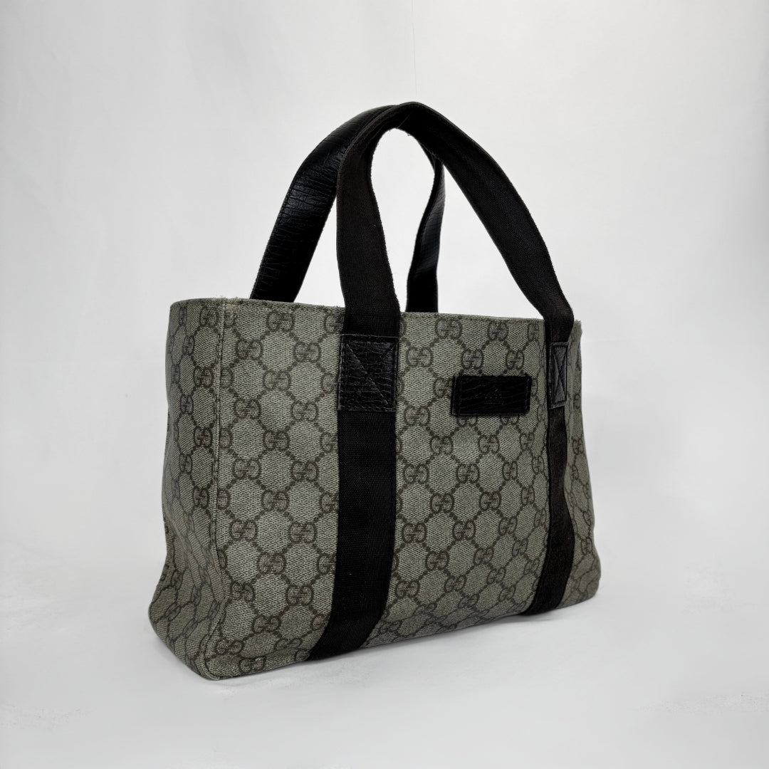 A vintage-style tote bag featuring a gray and black GG monogram canvas body with black leather handles and trim, set against a plain light gray background.
