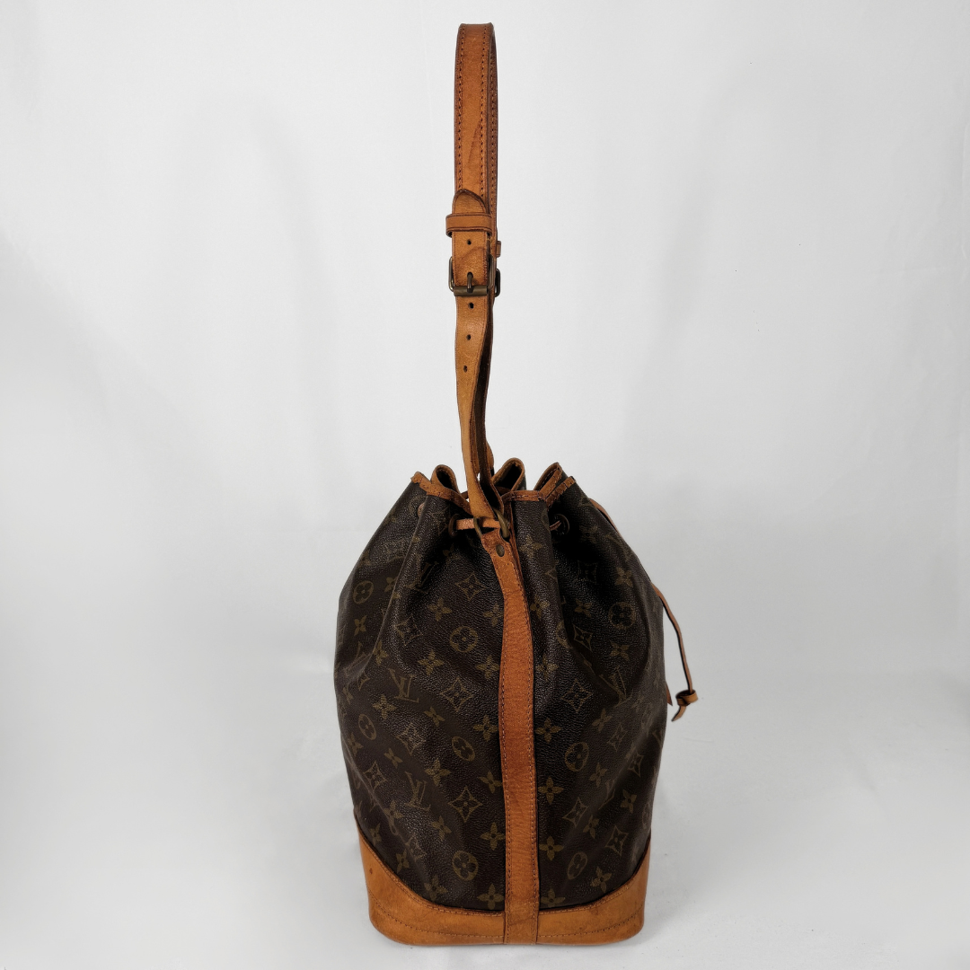 A vintage Louis Vuitton monogram canvas bucket bag with tan leather trim and a matching adjustable shoulder strap, photographed against a neutral light gray background.
