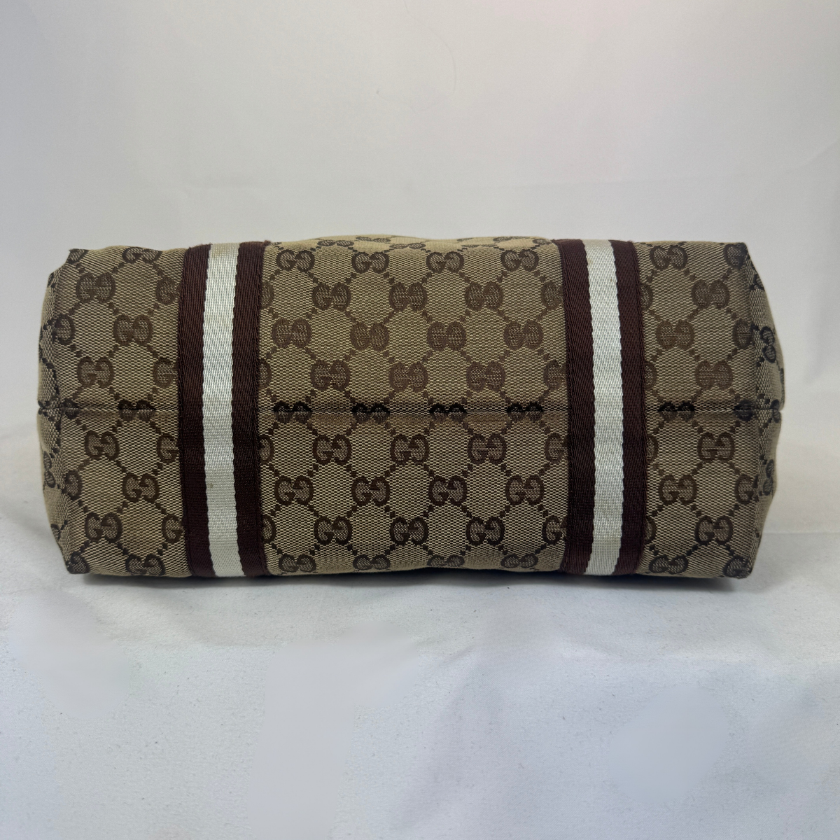 A Gucci canvas shoulder bag with the classic GG Supreme monogram pattern in beige and brown, featuring two vertical stripes of white and dark brown on the front.