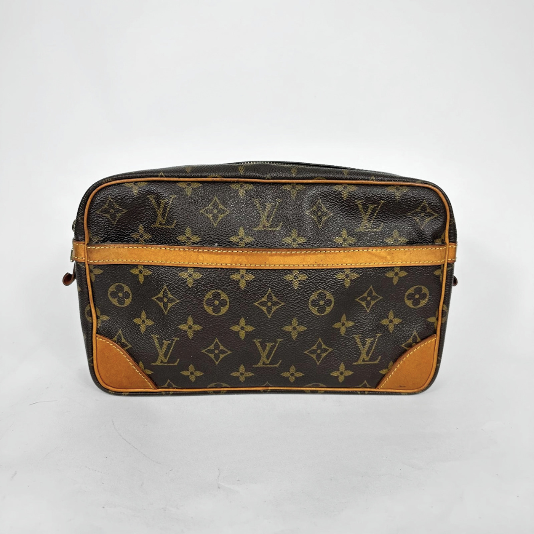A Louis Vuitton monogram canvas toiletry bag with brown leather trim and corner patches, photographed against a plain light gray background.