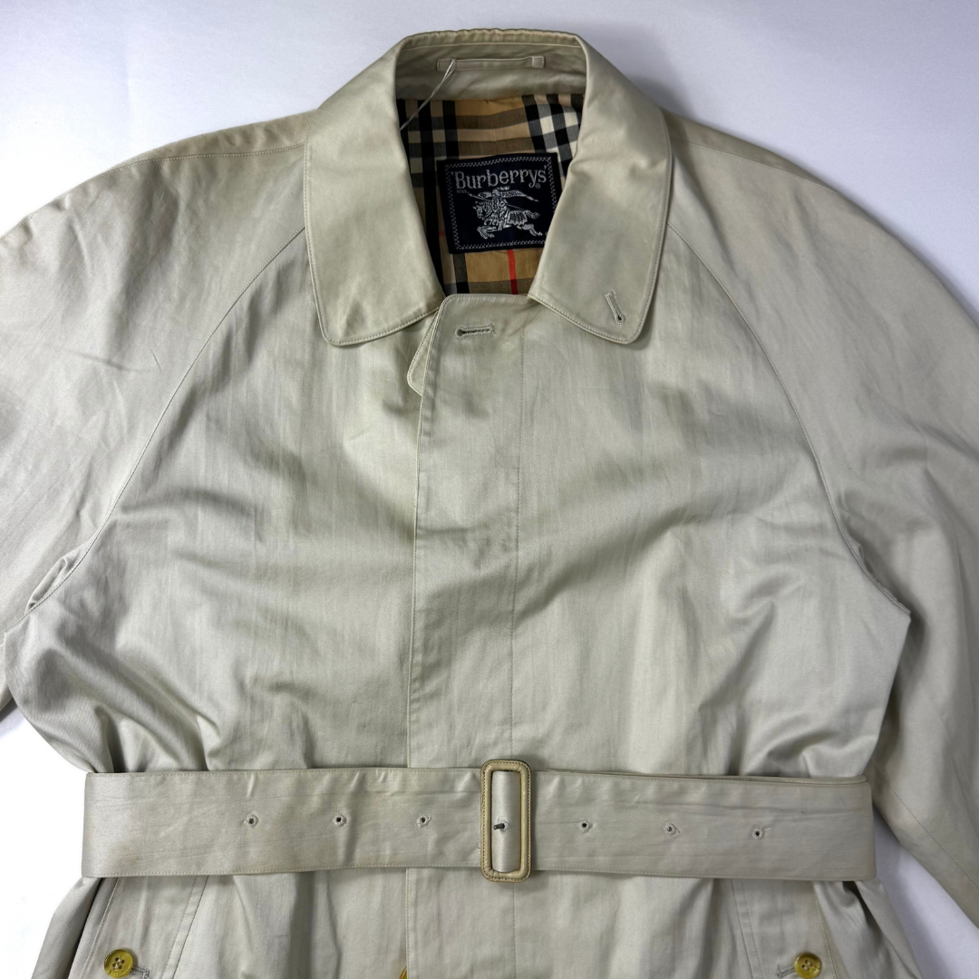 Beigefarbener Trenchcoat, getragen von einer Person vor weißem Hintergrund