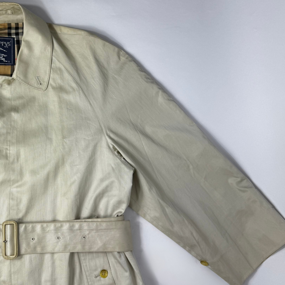 Beigefarbener Trenchcoat, getragen von einer Person vor weißem Hintergrund
