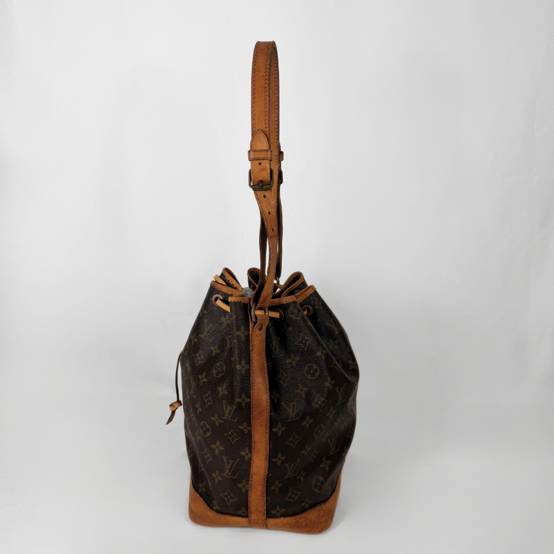 A Louis Vuitton monogram canvas bucket bag with tan leather trim and a single shoulder strap, photographed against a plain light gray background.