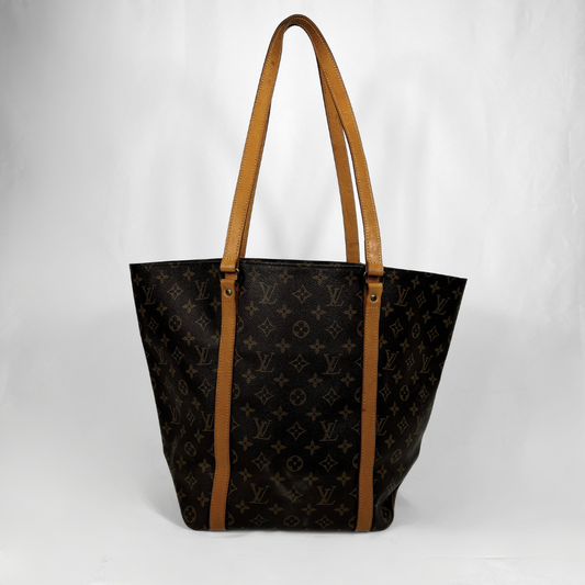 A Louis Vuitton Sac cabas en toile monogrammée noire avec bandoulières et finitions en cuir beige, photographié sur un fond gris clair uni.