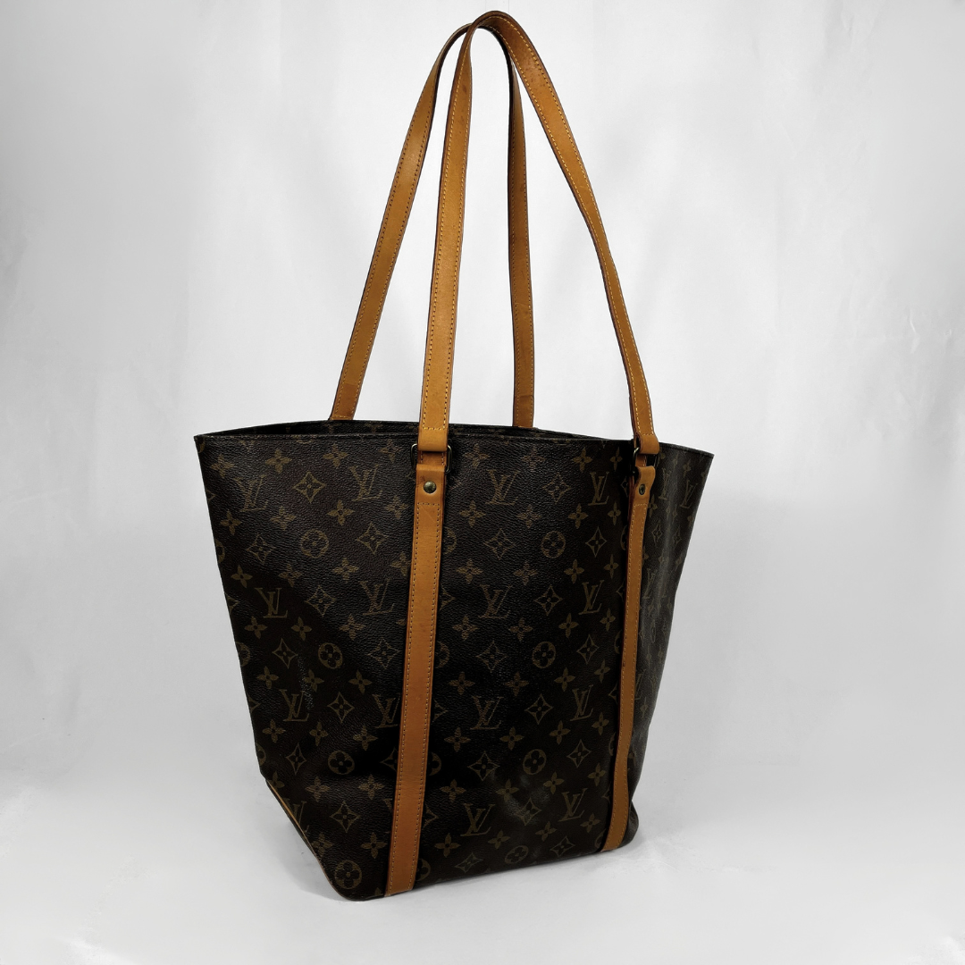 Louis Vuitton monogram canvas tote bag with tan leather shoulder straps and trim, shown on a white studio background.