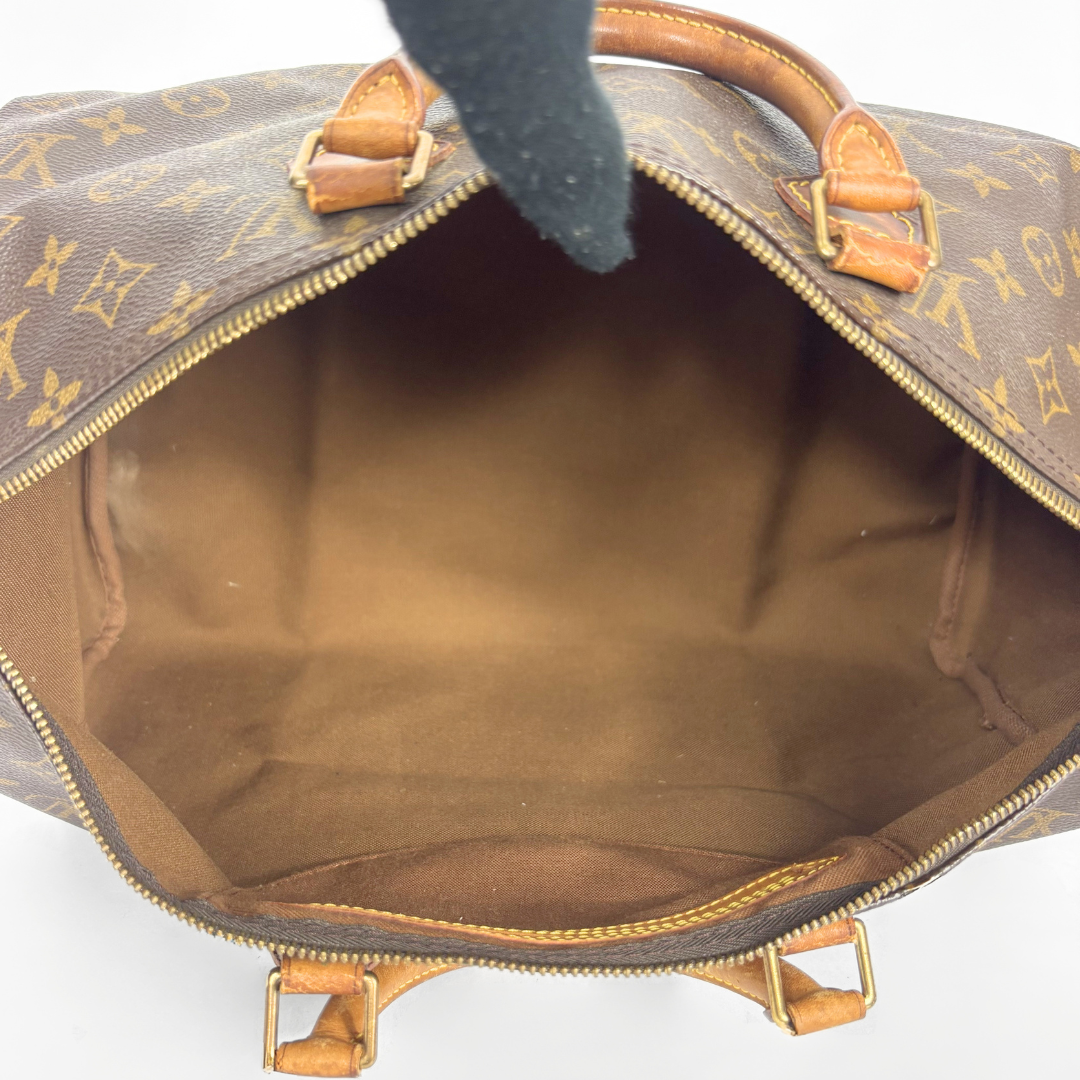 Offene braune Lederhandtasche mit goldenem Monogrammmuster auf weißem Hintergrund