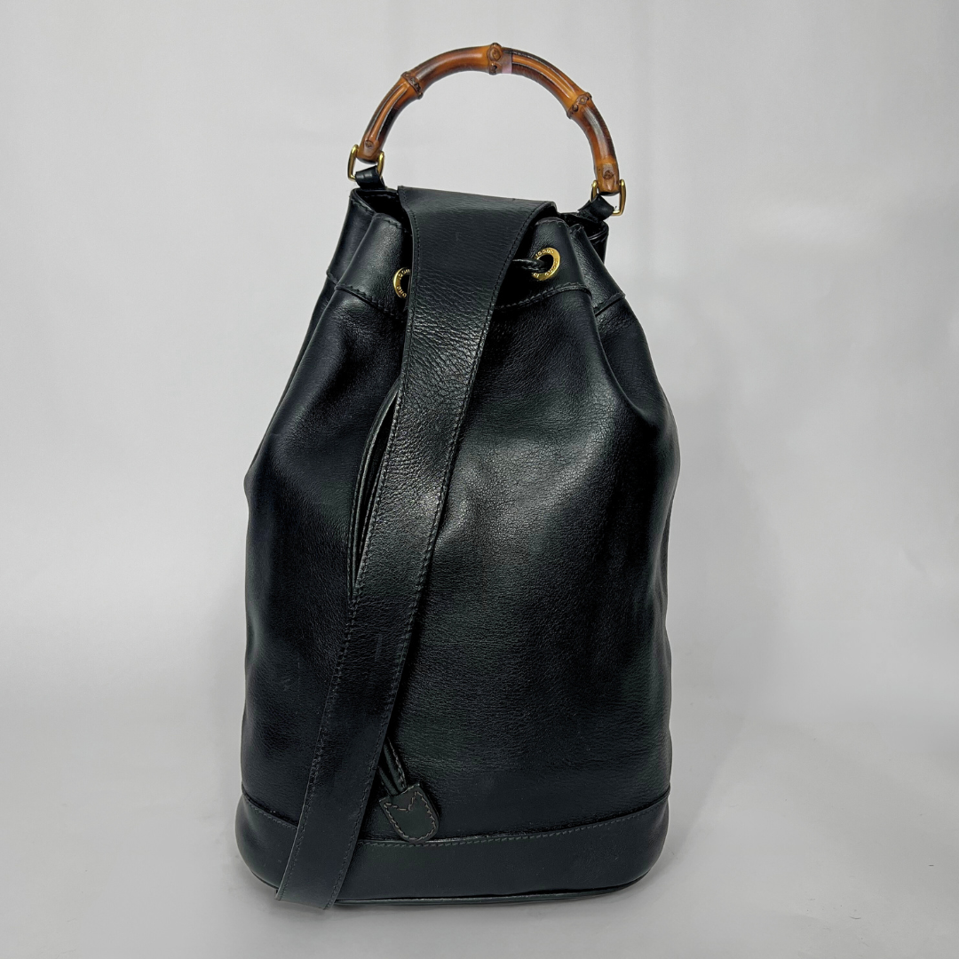 Mochila de couro preta com alça de bambu sobre fundo cinza.