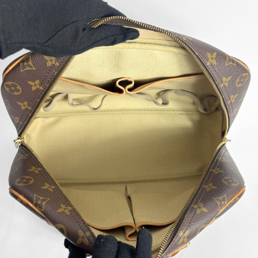 An open Louis Vuitton monogram toiletry bag or toiletry case, showing the beige interior lining and zip-around construction, with black-gloved hands holding it open against a plain white background.