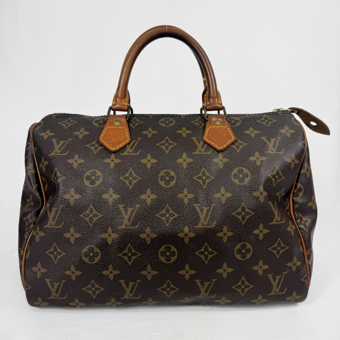 A Louis Vuitton monogram Speedy handbag in dark brown coated canvas with tan leather handles and trim, shown against a plain white background.