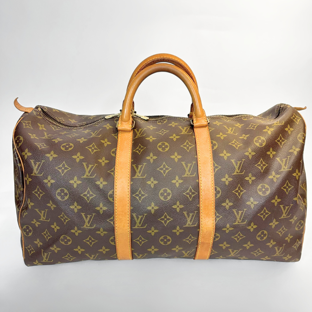 Bolso de viaje marrón con asas de cuero color canela sobre fondo gris claro.