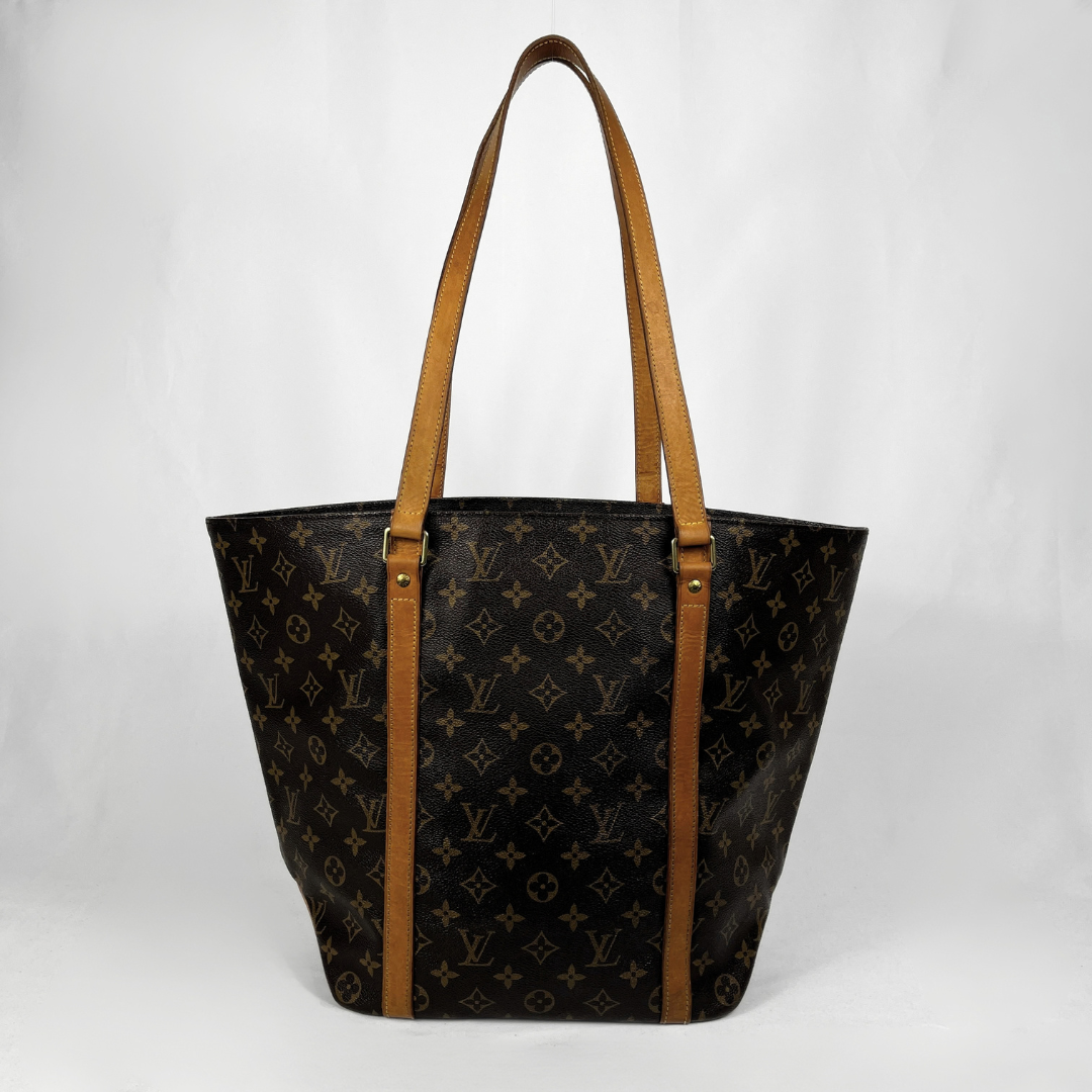 Louis Vuitton monogram canvas tote bag with tan leather shoulder straps and trim, photographed against a plain light gray background.