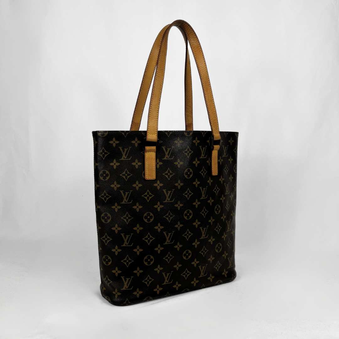 A Louis Vuitton monogram tote bag in black coated canvas with tan leather shoulder straps, photographed against a light gray studio background.