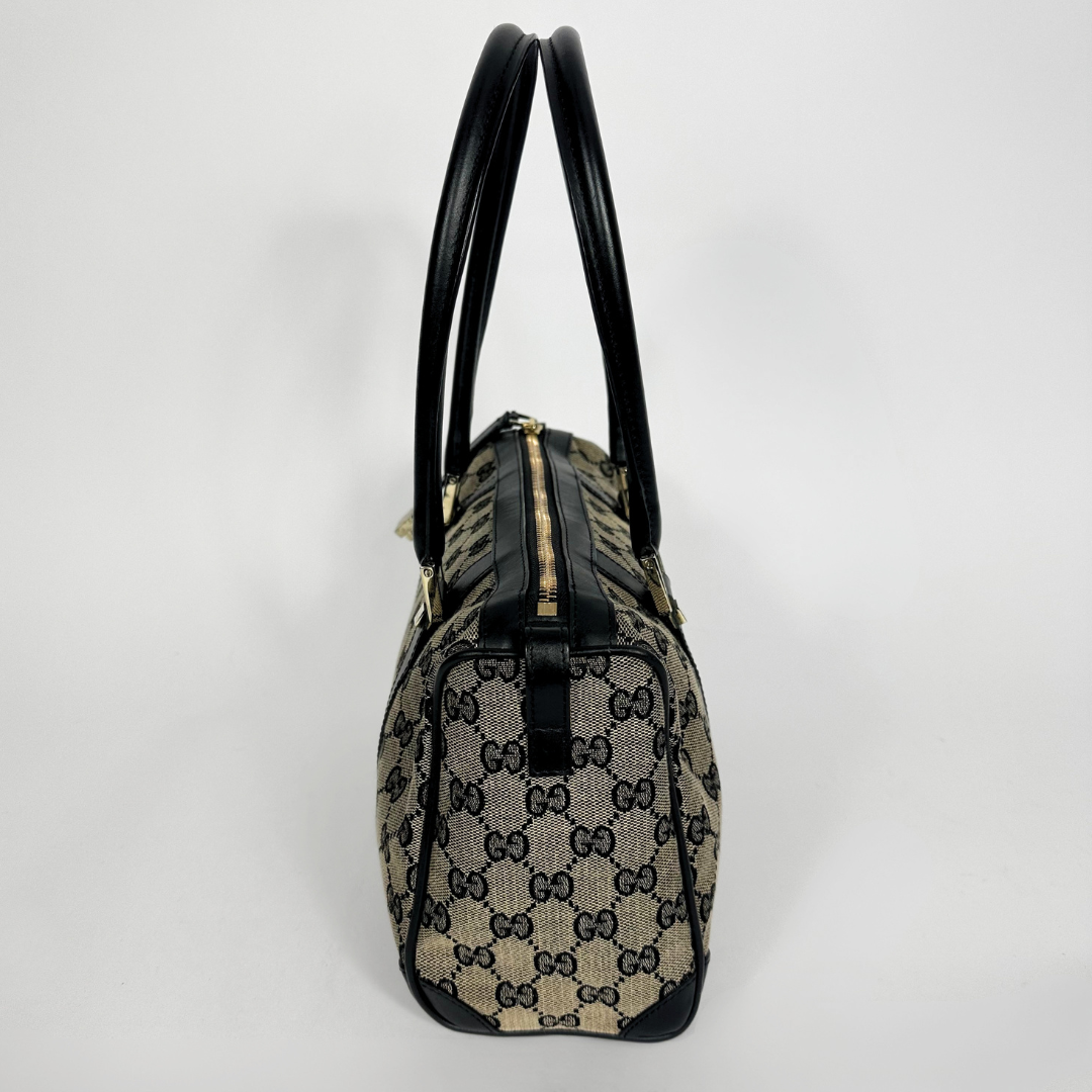 Designer handbag with black handles and trim on a light gray background