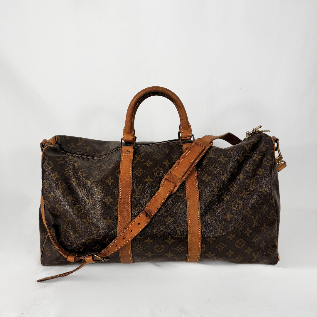 A Louis Vuitton monogram canvas duffel bag with brown leather handles and a matching shoulder strap, photographed against a plain light background.
