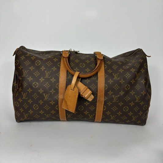 Brown monogram patterned duffel bag with tan leather straps on a white background
