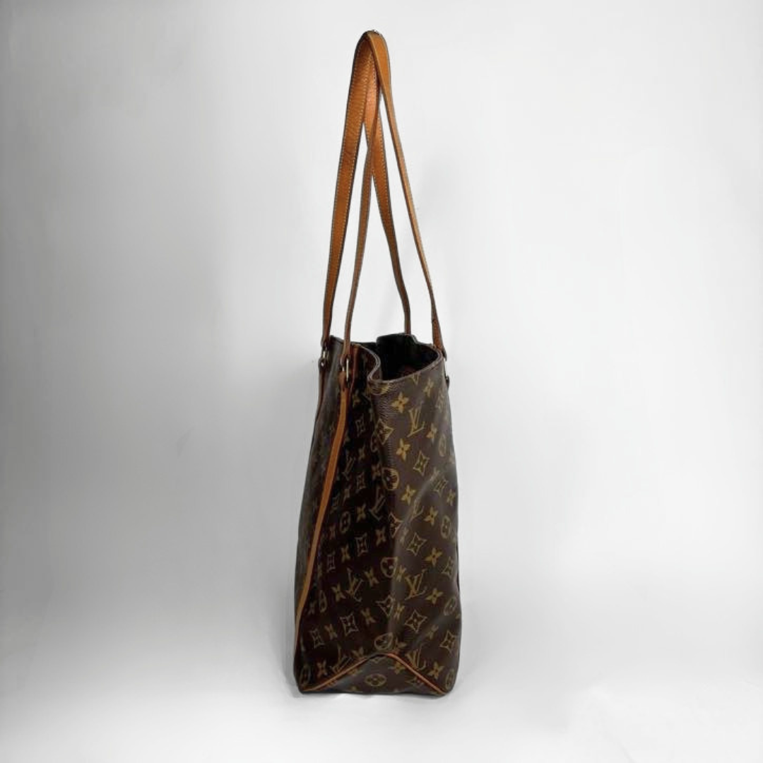 A Louis Vuitton monogram canvas tote bag in dark brown with tan leather shoulder straps, shown from a side profile view against a light gray studio background.