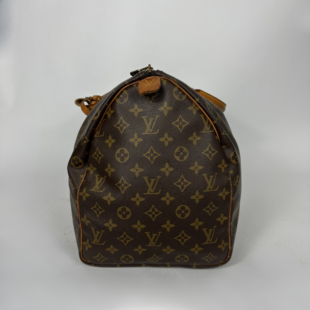 Brown monogram patterned duffel bag with tan leather straps on a white background