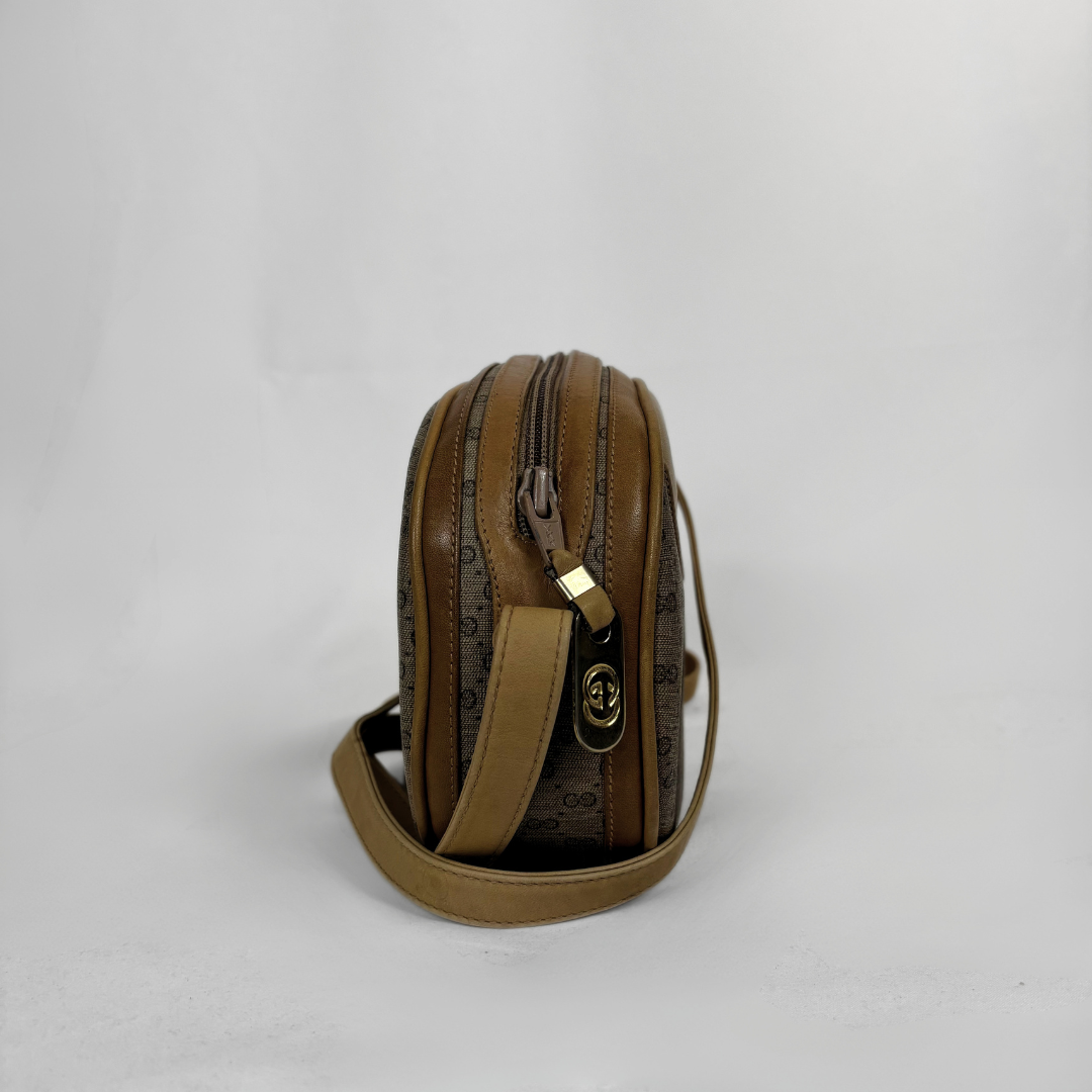 A brown leather crossbody bag with a repeating monogram pattern, featuring a gold-tone logo clasp and a matching leather strap, photographed against a light gray background.