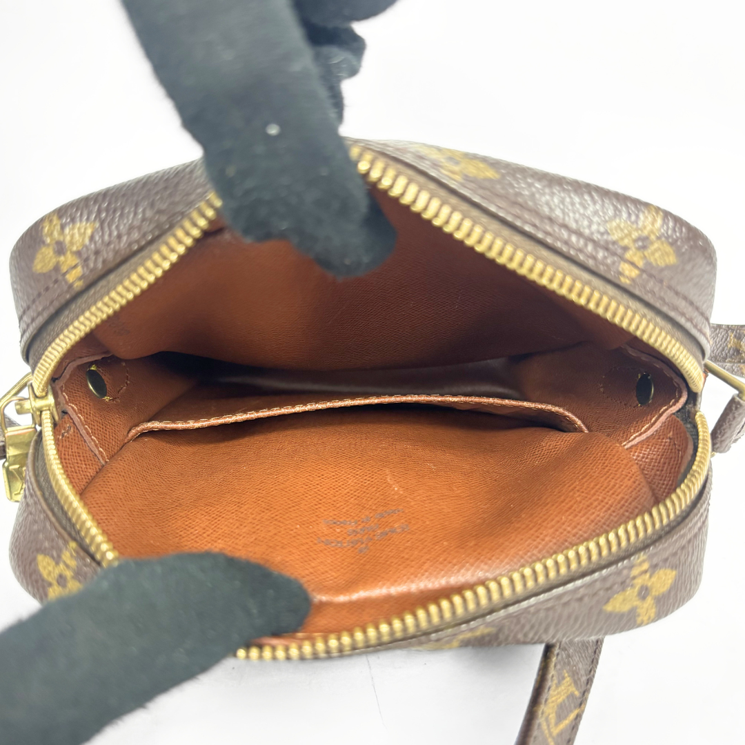 Brown handbag with gold accents being held open by a gloved hand on a white background