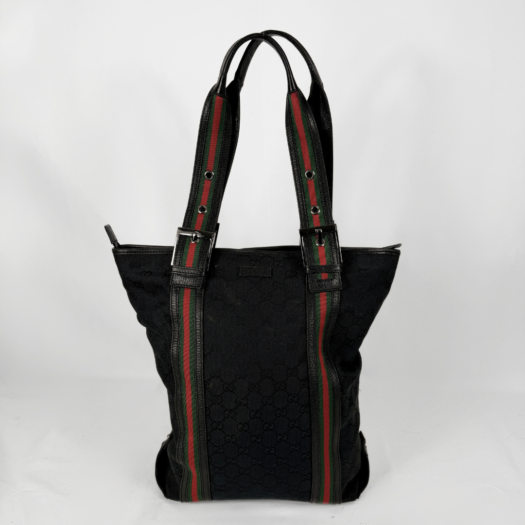 A black Gucci tote bag featuring the brand's signature green and red web stripe pattern on the handles and side panels, set against a plain white background.