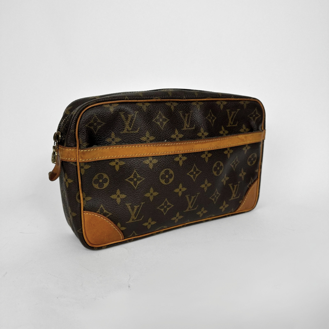 Louis Vuitton monogram canvas toiletry bag with tan leather trim and corner patches, photographed on a light gray background.