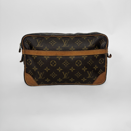 A Louis Vuitton monogram canvas pouch bag with brown leather trim and corner protectors, photographed against a neutral light gray background.