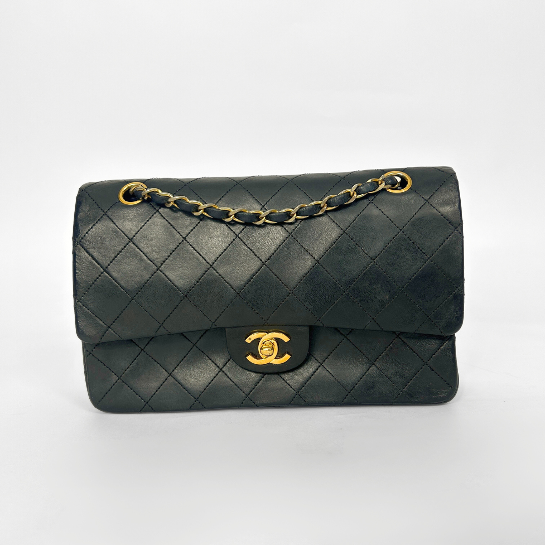 Black quilted handbag with gold chain and clasp on a white background