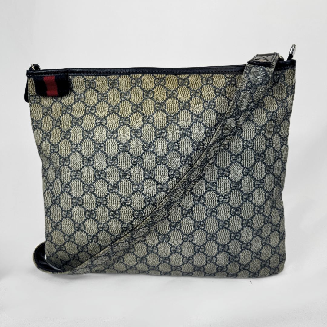 Gucci GG Supreme Web Flat Messenger bag in signature monogram canvas with green and red Web detailing and leather trims, displayed on a light grey background.