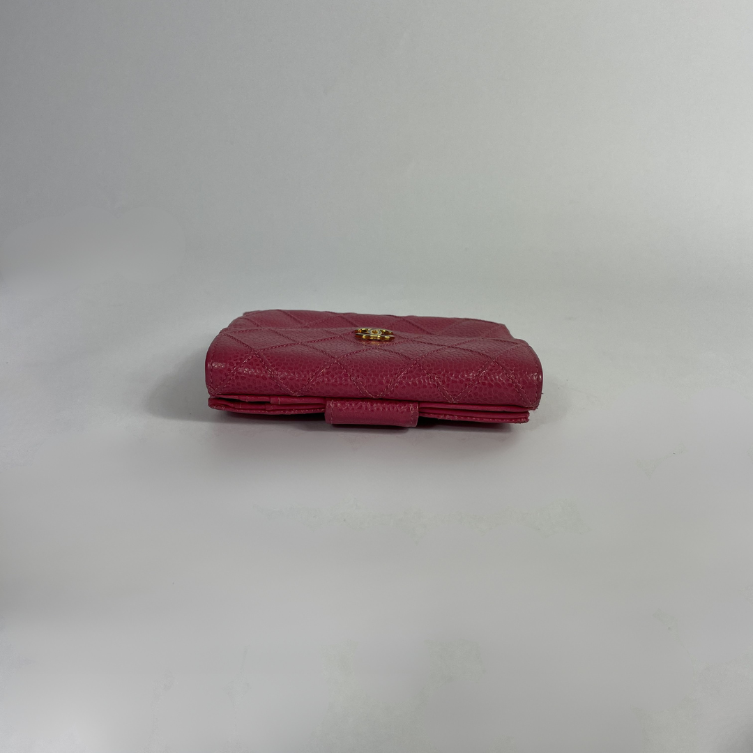 A small quilted leather clutch bag in a deep magenta pink, featuring a gold-tone logo clasp on a plain light gray background.