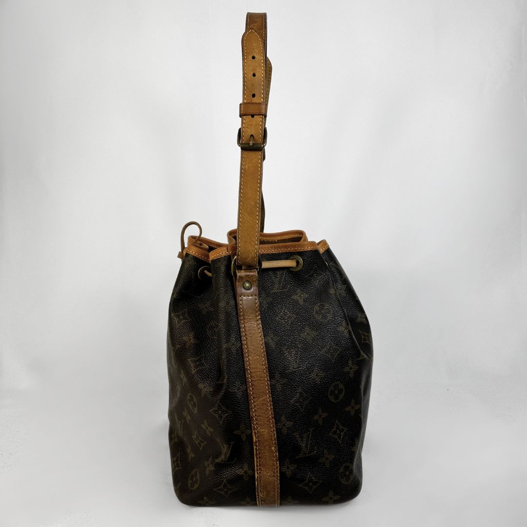 A Louis Vuitton monogram canvas bucket bag with tan leather trim and a matching shoulder strap, photographed against a plain light gray background.