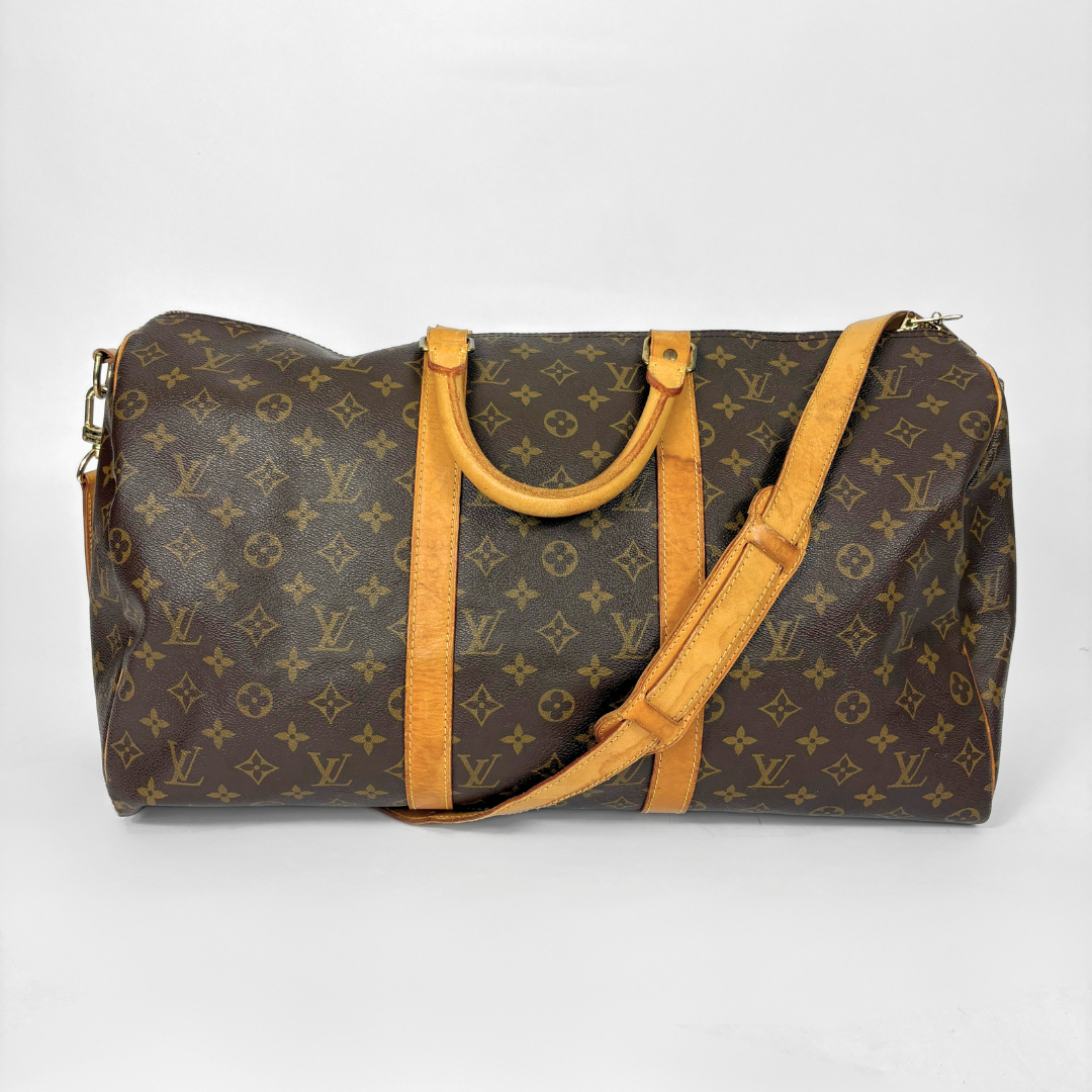Louis Vuitton monogram travel bag with brown handles and strap on a white background
