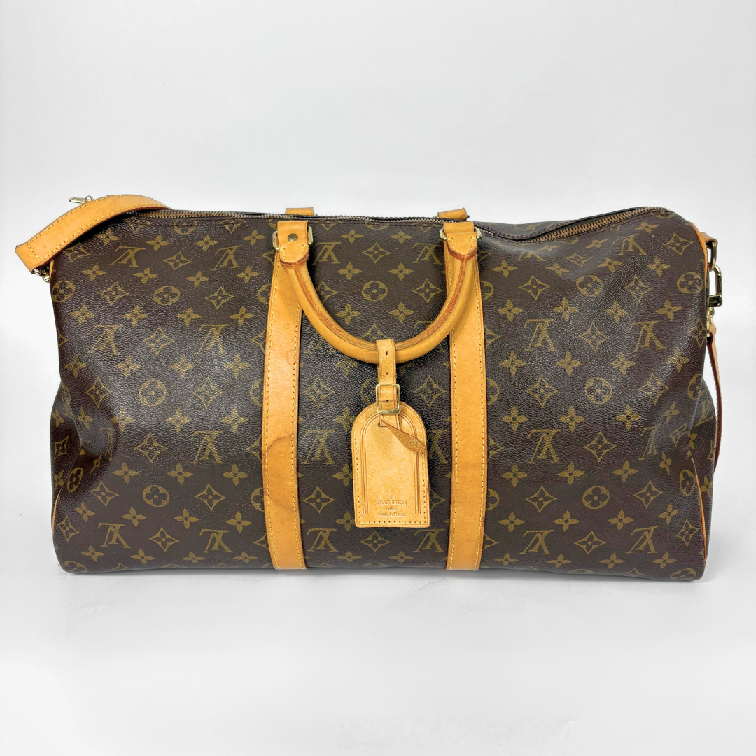 Louis Vuitton monogram travel bag with brown handles and strap on a white background