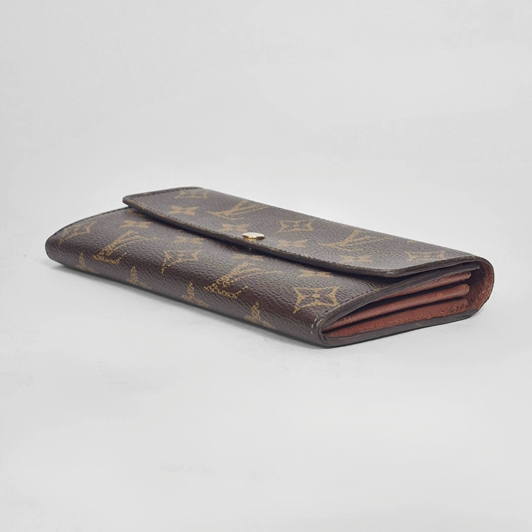 Folded brown leather wallet with gold monogram pattern on a light gray background