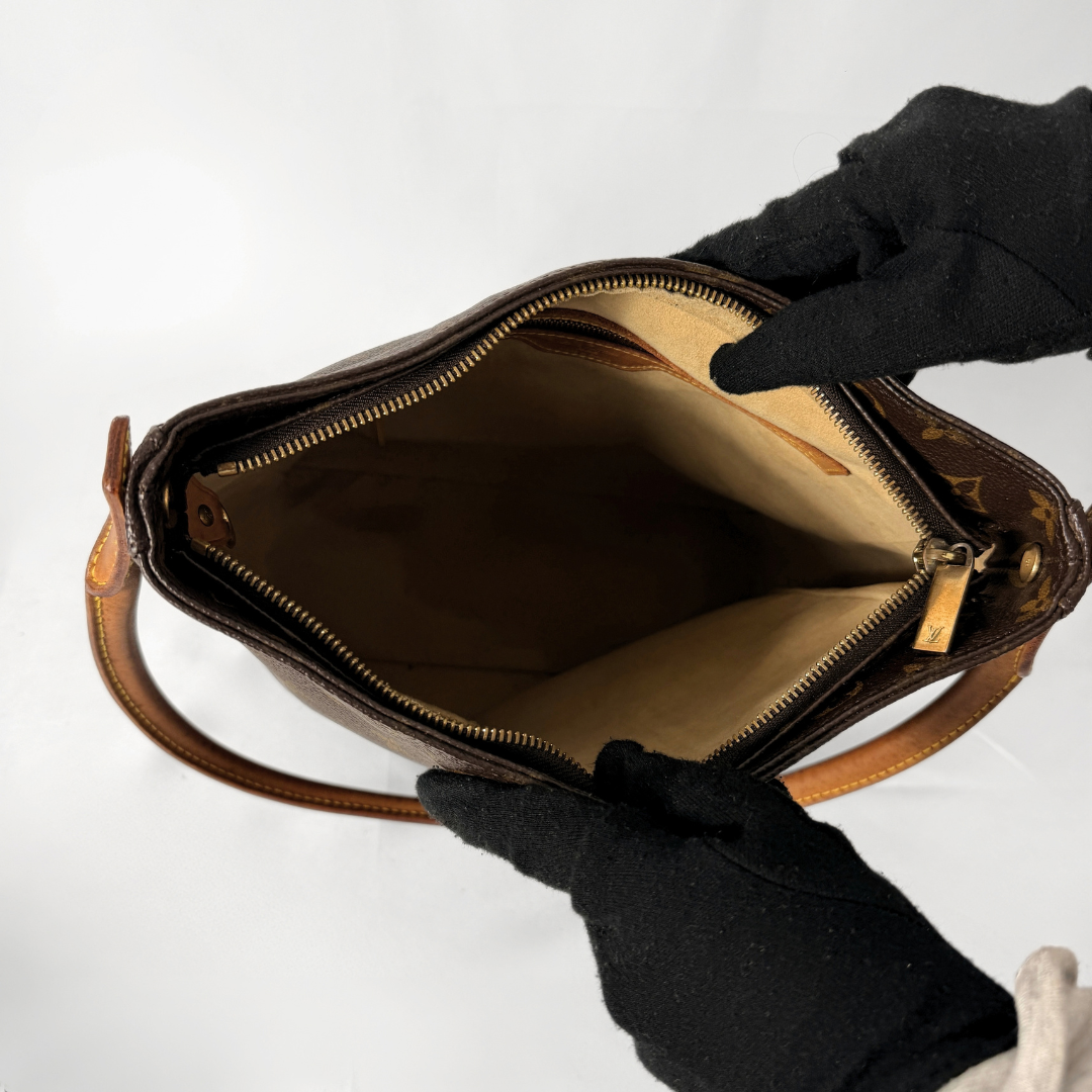 A brown Louis Vuitton monogram handbag shown open, with a person wearing black gloves holding it to display the interior. The beige lining and gold-toned zipper are visible against a plain white background.