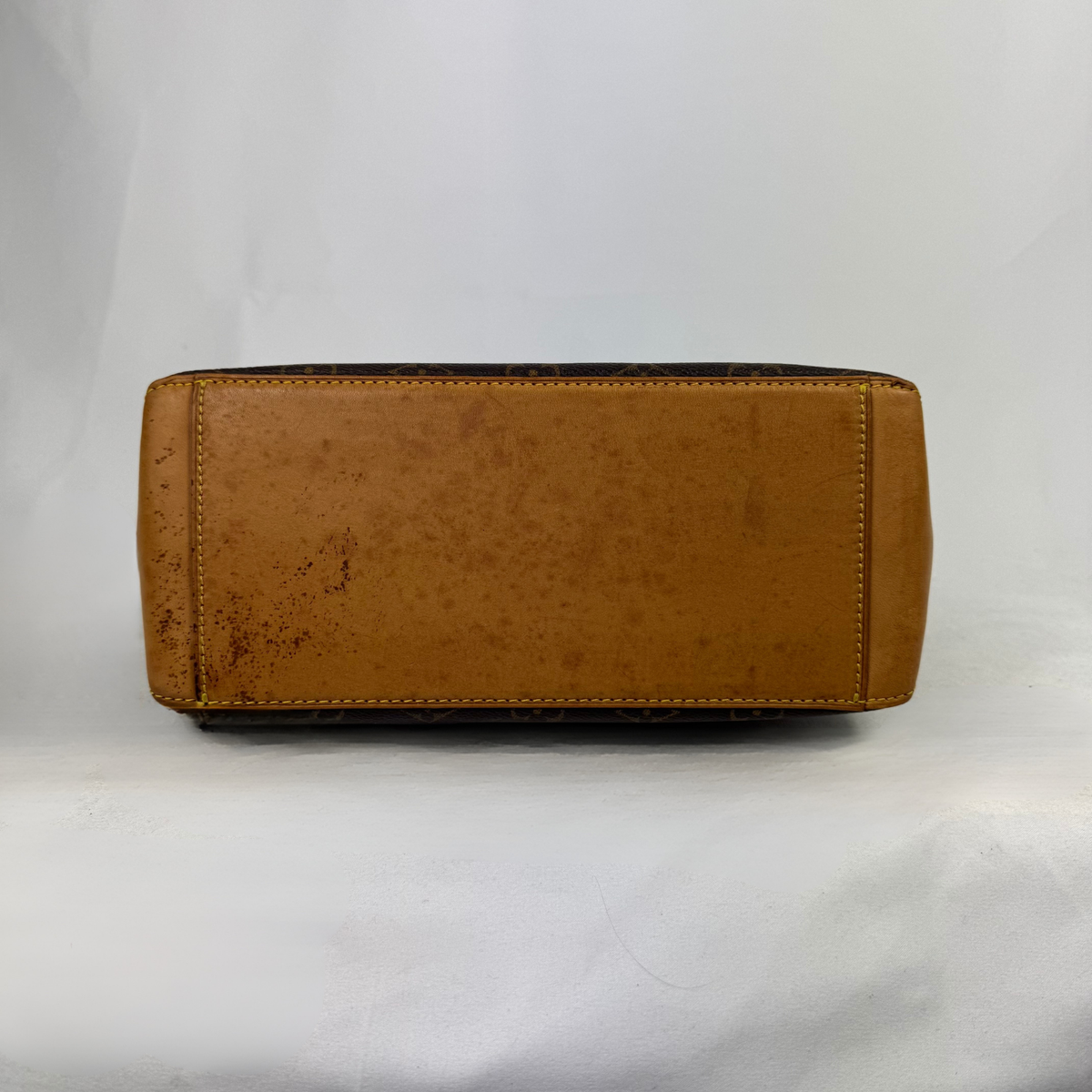 A tan ostrich leather handbag shown from the bottom, displaying its stitched edges and textured surface, set against a plain white backdrop.