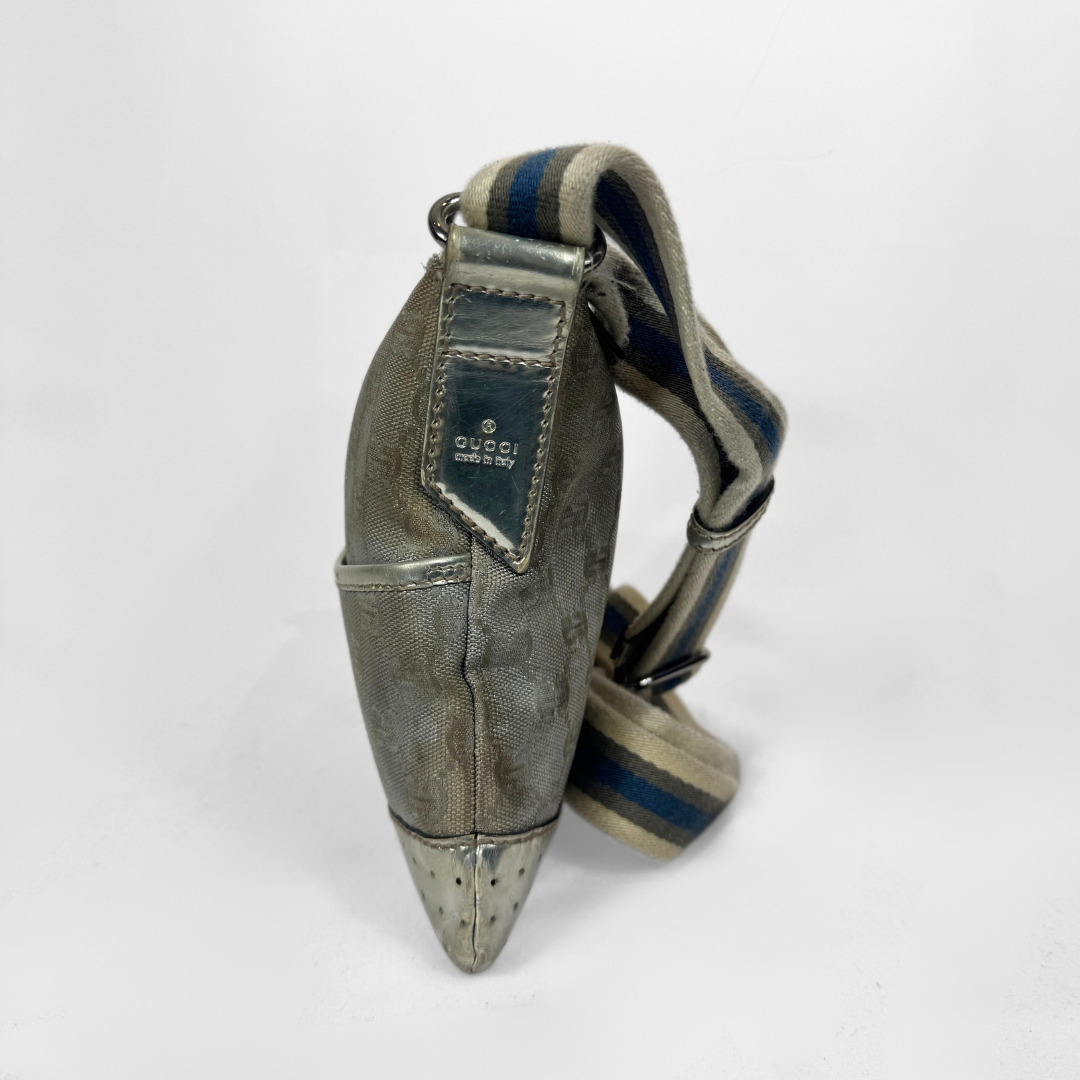 A Gucci GG canvas crossbody bag in metallic silver with a blue and beige striped shoulder strap, silver-tone hardware and a studded base, photographed against a plain white background.