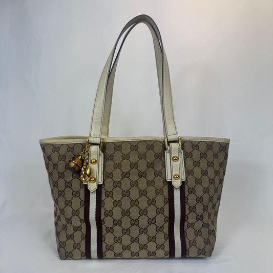 A Gucci tote bag in the classic GG Supreme canvas, featuring beige and brown monogram pattern, cream-colored leather handles, and gold-tone hardware.